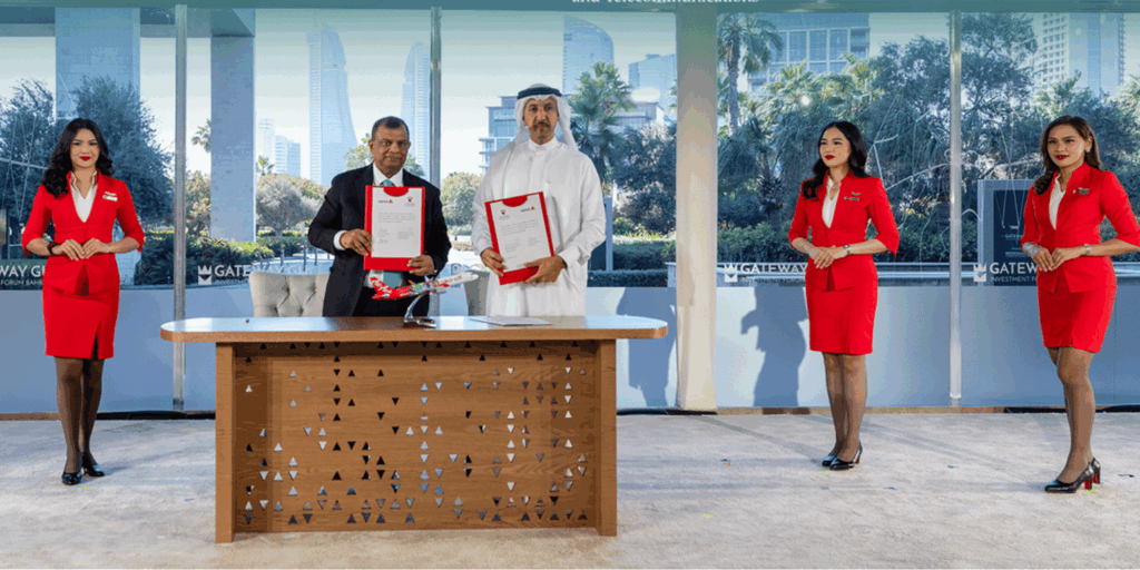 Tony Fernandes and Bahraini officials seated at formal ceremony table during agreement signing in Manama, Bahrain, with branding banners and documents visible